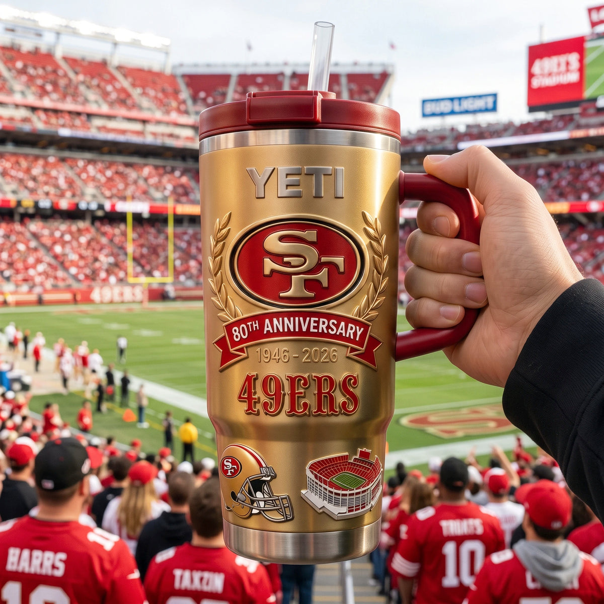 Gold 49ers anniversary tumbler with red handle and straw held above a football stadium