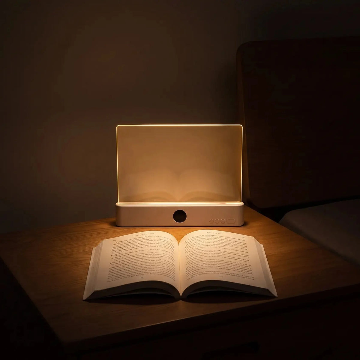 A rectangular LED night light glowing warmly on a wooden bedside table, with an open book placed in front of it in a dimly lit bedroom.